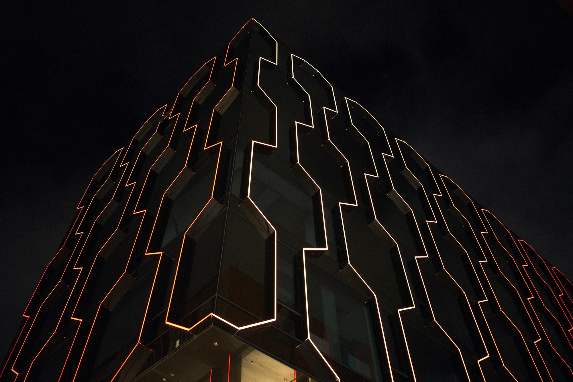 Linear lighting tracing the angular panels of a dark building facade at night